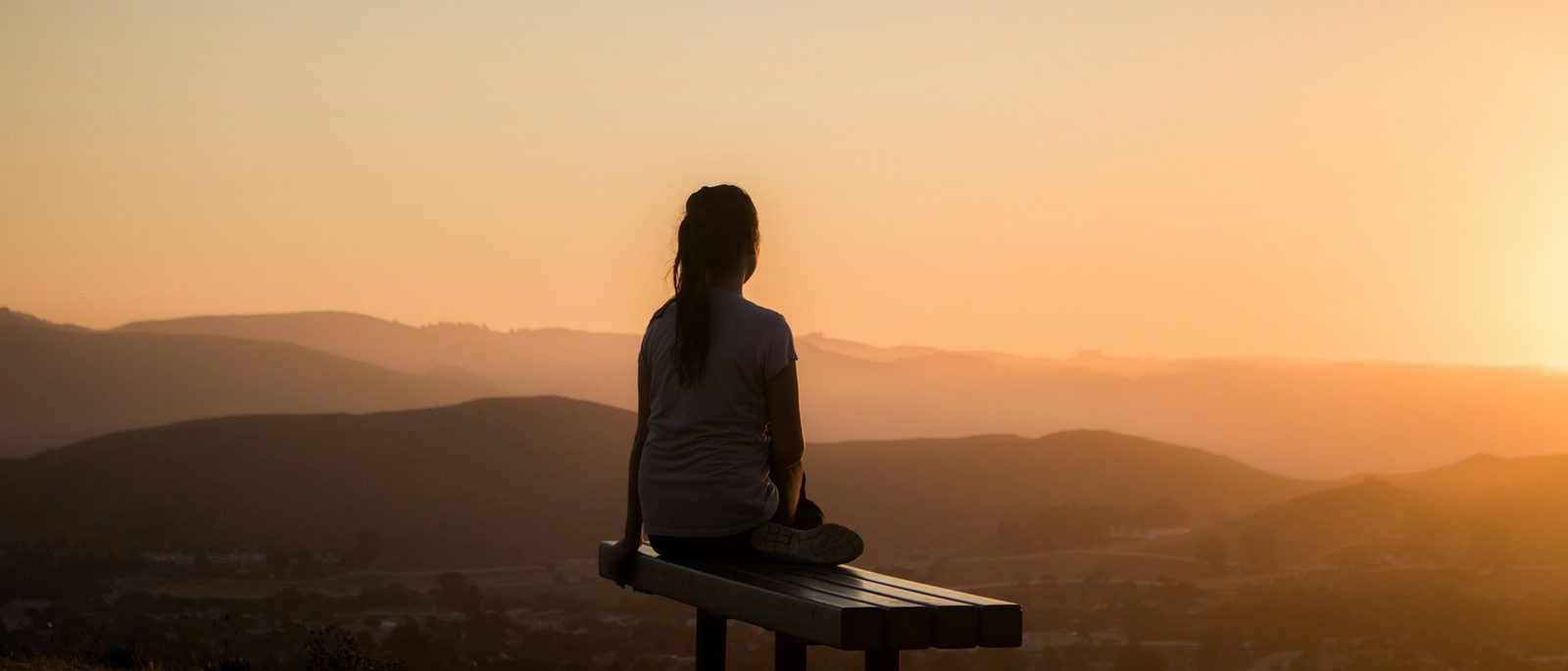Une femme assise face aux montagnes au crépuscule
